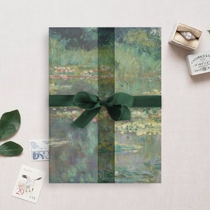 May include: A green and blue painting of water lilies is wrapped in green paper with a green ribbon. The painting is tied with a green ribbon and bow. The painting is on a white background.