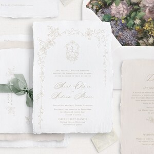 Pu&ograve; includere: Un set di inviti di nozze con sfondo bianco e calligrafia dorata. L'invito presenta un design floreale e i nomi "Sarah Olsen" e "Andrew Mason". La carta dei dettagli include informazioni sul luogo del matrimonio, Greencrest Manor, e dettagli sulla sistemazione.