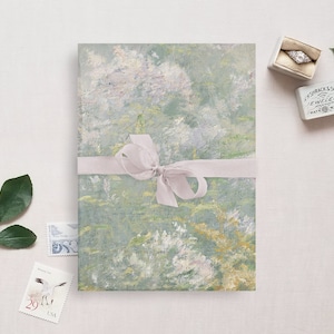 May include: A green and white patterned paper with a light pink ribbon tied in a bow. The paper is wrapped around a gift box. The box is sitting on a white surface.