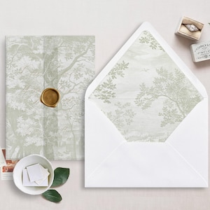 Può includere: Un set di partecipazioni di nozze con una busta bianca con un motivo a forma di albero all'interno. L'invito ha un design ad albero abbinato ed è sigillato con un sigillo di cera dorata. Sono presenti anche un portagioie, francobolli e verde.
