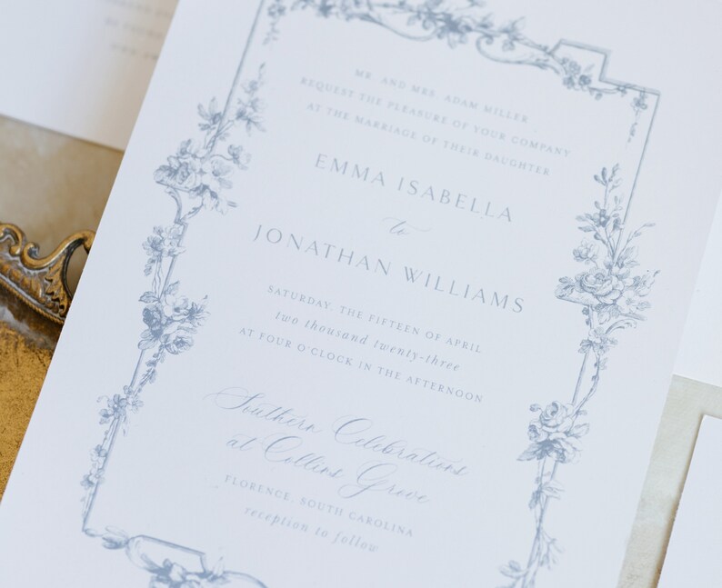 May include: A wedding invitation with a blue floral border. The invitation reads "Mr. and Mrs. Adam Miller request the pleasure of your company at the marriage of their daughter Emma Isabella to Jonathan Williams Saturday, the fifteen of April two thousand twenty-three at four o'clock in the afternoon Southern Celebrations at Collins Grove Florence, South Carolina reception to follow"