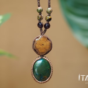 May include: A macrame necklace featuring a brown cord with two dark brown beads, two mottled green and brown beads, a circular wooden flower-shaped pendant, and a large oval green stone pendant. The text ITAYA ARTE is visible in the bottom right corner.
