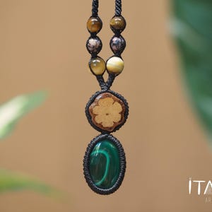 May include: A necklace featuring a black cord with macrame knots, brown and tan beads, a circular wooden piece with a flower-shaped cutout, and an oval green malachite stone pendant. The text ITAYA ARTE is visible in the bottom right corner.