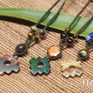 May include: Three macrame necklaces featuring gear-shaped stone pendants in red, green, and beige, accented with round tiger eye and lapis lazuli beads on braided cords. The text ITAYA is visible in the bottom right corner of the image.