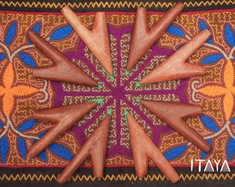 May include: A collection of ten wooden, Y-shaped tools arranged in a circular pattern. The tools are a warm brown color and rest on a colorful, patterned textile with orange, purple, and blue hues. The word "ITAYA" is visible in the bottom right corner.
