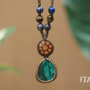 May include: A macrame necklace featuring a teardrop-shaped green malachite pendant, a circular patterned wooden bead, and smaller round blue, brown, and grey stone beads strung on a brown cord. The text ITAYA ARTE is visible in the corner.