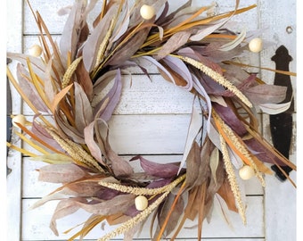 May include: A dried floral wreath with beige, brown, and purple leaves and white berries. The wreath is hanging on a white wooden door.