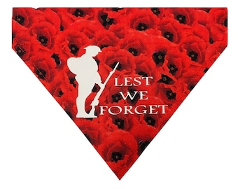 May include: A triangular pet bandana featuring a vibrant red poppy flower pattern. A white silhouette of a soldier holding a rifle stands on the left side, accompanied by the white text LEST WE FORGET printed clearly on the right side of the fabric.