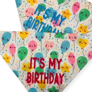 May include: Two white dog bandanas with a colorful balloon pattern. The bandanas have the text "It's My Birthday" in blue and red lettering.