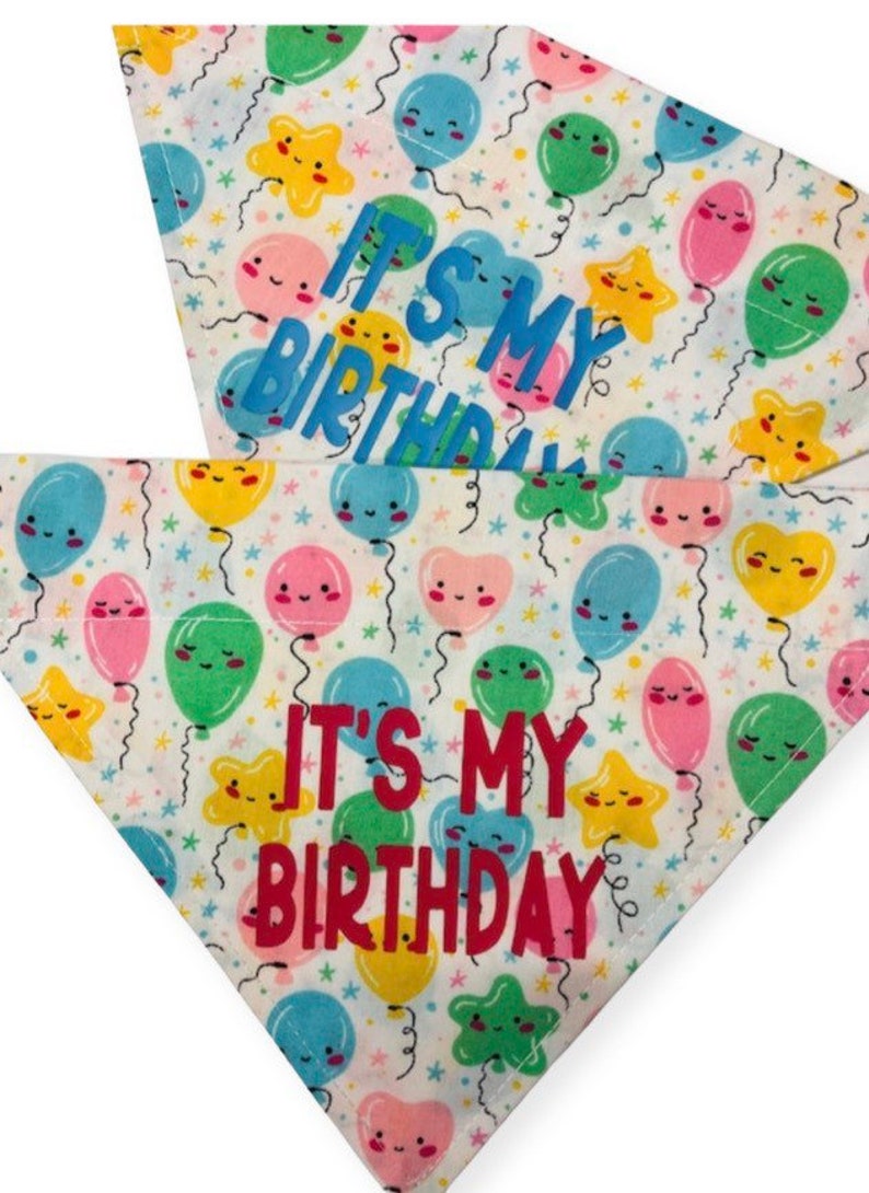 May include: Two white dog bandanas with a colorful balloon pattern. The bandanas have the text "It's My Birthday" in blue and red lettering.