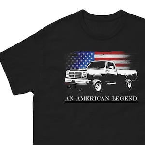 May include: Black t-shirt with a white silhouette of a pickup truck driving in front of an American flag. The text "An American Legend" is printed below the truck.