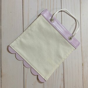 May include: A small, white canvas bag with a lavender scalloped edge and a lavender faux leather top. The bag has two metal eyelets and a white rope handle.
