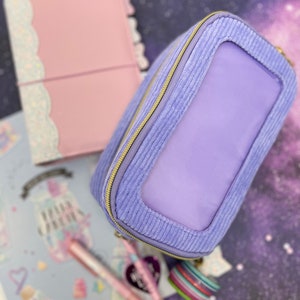 Può includere: Una pochette con zip in velluto a coste lavande con una finestra in plastica trasparente. La pochette ha una zip dorata ed è perfetta per riporre piccoli oggetti.