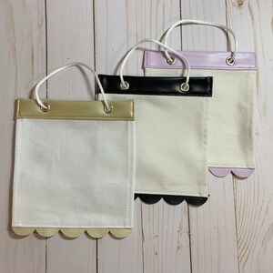 May include: Three white fabric pouches with scalloped edges and different colored faux leather trim. The pouches have a gold, black, and purple trim.