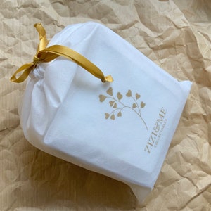 May include: A white drawstring bag with a gold ribbon and a gold logo that says "Zizzi & Me  Collectibles". The logo is a stylized branch with gold hearts.