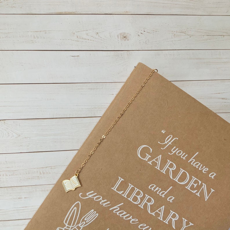 May include: A brown notebook with a gold chain bookmark with a white open book charm. The notebook has the text "If you have a GARDEN and a LIBRARY you have everything" printed on the cover.