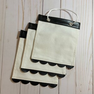 May include: Three white fabric pouches with black scalloped edges and black leather trim. Each pouch has a white string loop handle.
