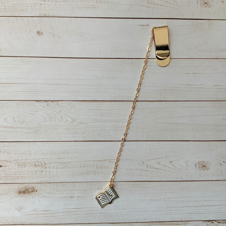 May include: Gold bookmark with a chain and a book charm. The book charm is open and has a white background with black lines.