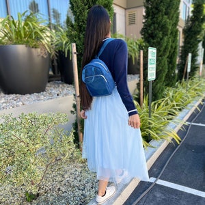 Puede incluir: Una mujer con un suéter azul y una falda de tul azul claro lleva una pequeña mochila de mezclilla azul.