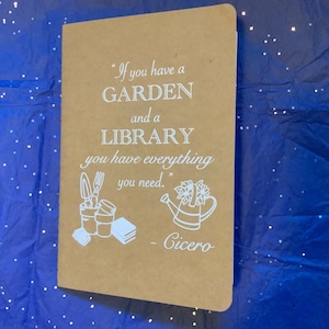 Peut inclure: Un carnet brun avec une citation blanche qui dit "Si vous avez un JARDIN et une BIBLIOTHÈQUE, vous avez tout ce dont vous avez besoin." La citation est attribuée à Cicéron. Le carnet a une illustration blanche d'un arrosoir et d'outils de jardinage.