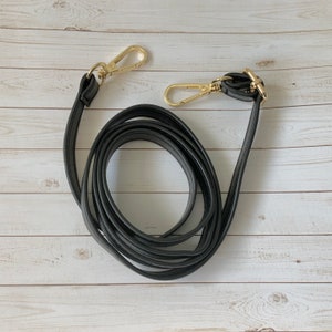 May include: Black leather strap with gold-toned clasps. The strap is coiled and ready to be attached to a bag.