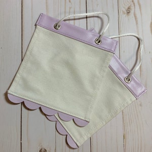May include: Two white fabric banners with scalloped edges and lavender trim. The banners have grommets and are attached with white string.