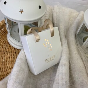 May include: White gift bag with gold handles and a gold floral design. The bag has the text "Zizzi & Me Collectables" printed on the front.