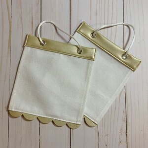 May include: Two white fabric banners with gold trim and scalloped edges. The banners have gold eyelets and are ready to be hung.