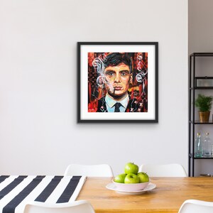 Puede incluir: Una pintura enmarcada de un hombre con cabello oscuro y traje, fumando un cigarrillo. El fondo es un dise&ntilde;o abstracto rojo y negro con humo blanco.