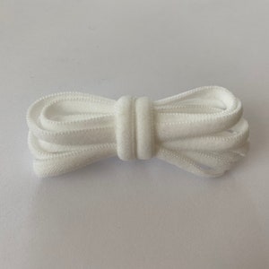 Pode incluir: Cord&atilde;o el&aacute;stico branco, dobrado ao meio, com textura lisa. O cord&atilde;o tem aproximadamente 1,2 cm de largura.