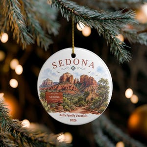 Puede incluir: Un adorno de cerámica blanca redonda con un paisaje pintado de Sedona, Arizona, que muestra formaciones rocosas rojas, un letrero de bienvenida y una pequeña capilla de piedra. El texto dice SEDONA arriba y Kelly Family Vacation 2026 abajo.