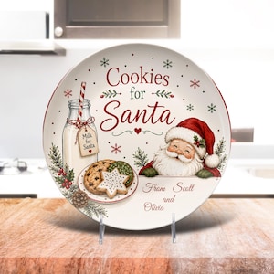 May include: A round white ceramic plate featuring the text Cookies for Santa in red and green script. The design includes a glass bottle of milk with a red and white striped straw, a plate of cookies, a smiling Santa Claus, and the text From Scott and Olivia.
