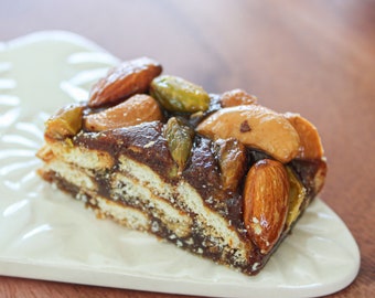 May include: A close-up of a slice of layered dessert with a chocolate base and topped with almonds, cashews, and pistachios.