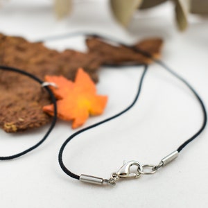May include: A black cord necklace with a silver clasp and an orange maple leaf charm.