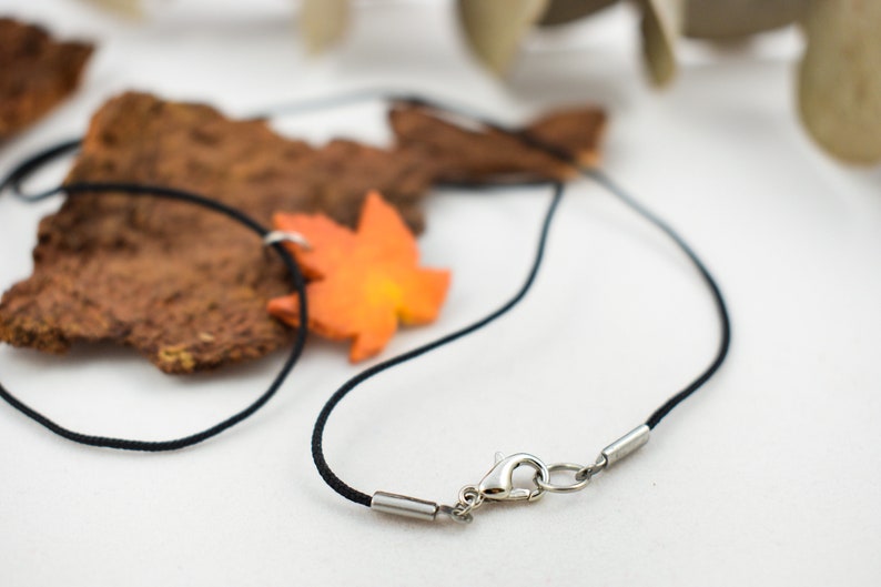 May include: A black cord necklace with a silver clasp and an orange maple leaf charm.