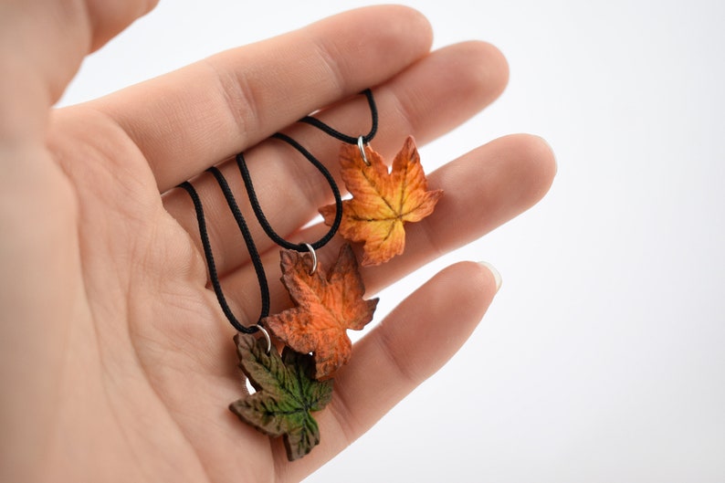 May include: Three necklaces with fall-colored leaf pendants. The leaves are made of polymer clay and are in shades of orange, red, and green.