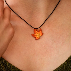 May include: A necklace with a pendant shaped like an orange and yellow maple leaf.