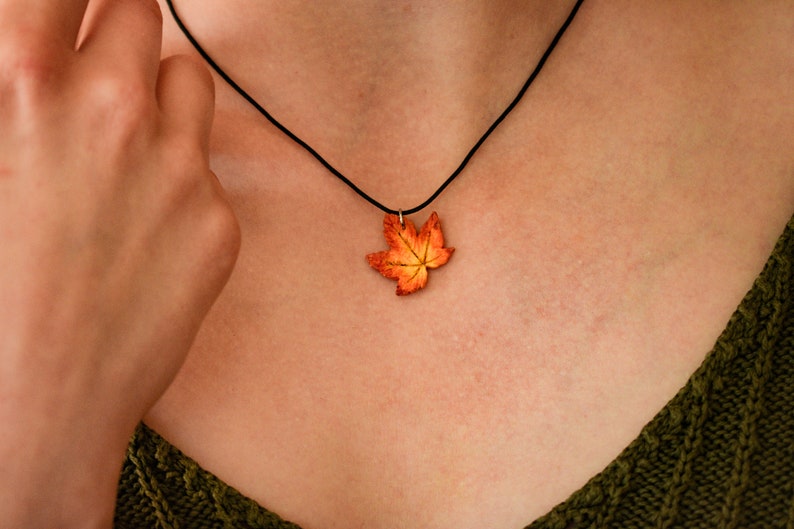 May include: A necklace with a pendant shaped like an orange and yellow maple leaf.