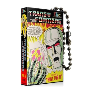 Puede incluir: Una portada de cinta VHS vintage con la caricatura de Transformers. La portada es negra con texto rojo y amarillo que dice "The Transformers" y "Vol. 6". La imagen muestra a Megatron sosteniendo un cubo con ojos rojos y una expresión amenazante. El texto en la portada dice "More Than Meets The Eye" y "And Now With A Single Anti-Matter Cube, I Will Destroy The Autobots!" La portada también incluye el texto "Volume 6 "Roll For It!"