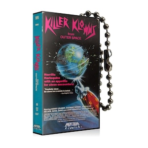 May include: A VHS tape keychain featuring the movie "Killer Klowns from Outer Space". The keychain is blue and black with a picture of a clown holding a rocket and a globe with a red and yellow explosion. The text "Killer Klowns from Outer Space" is in pink and black letters.