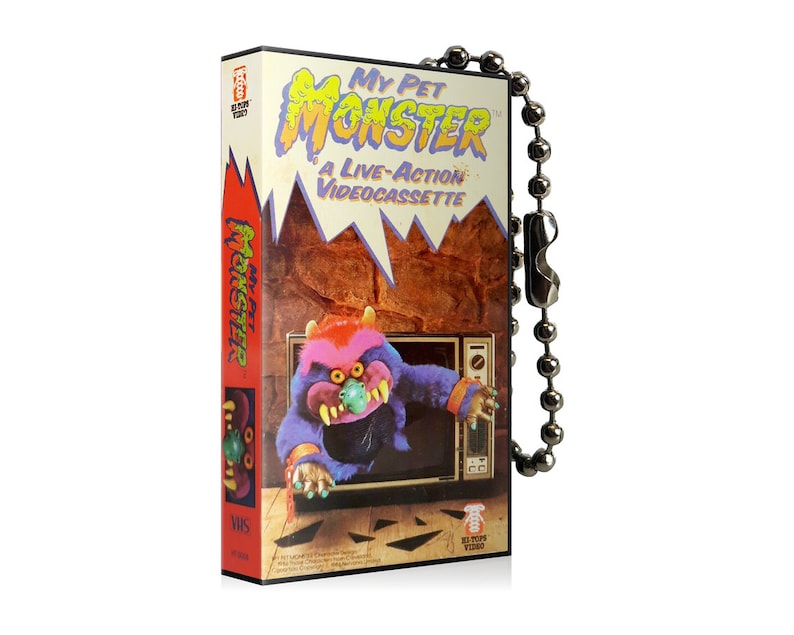 May include: A novelty VHS tape-shaped keyring with the text "My Pet Monster: A Live-Action Videocassette." The design includes a cartoon monster emerging from a television set. The keyring has a silver ball chain.