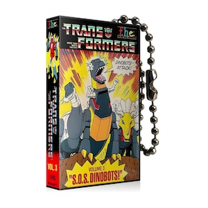 May include: A keychain featuring a vintage VHS tape design with a comic book style image of the Transformers Dinobots. The text on the tape reads "The Transformers Volume 3 "S.O.S. Dinobots!" VHS."
