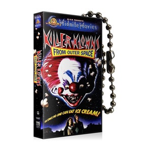 May include: A black VHS tape keychain with a scary clown face on the cover. The text on the cover reads "Killer Klowns from Outer Space". The keychain is attached to a silver chain.