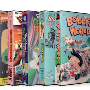 May include: A collection of VHS tapes featuring various cartoon characters, including Doug, Dino Riders, Bugs Bunny, BraveStarr, and Bobby's World. The tapes are arranged in a row, with the titles and logos visible.