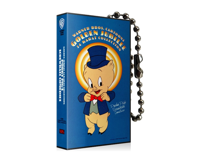 May include: A blue VHS tape featuring Porky Pig from Warner Bros. Cartoons' Golden Jubilee collection. The tape has a silver ball chain attached. The cover art includes Porky Pig in a top hat and bow tie.
