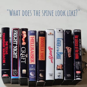 May include: A row of eight VHS tapes with various horror and action movie titles, including "The Texas Chainsaw Massacre", "Fright Night", "The Craft", "Hellraiser", "Godzilla 1985", "Strange Brew", "Father of the Bride", and "The Silence of the Lambs".