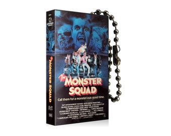 May include: A black VHS tape keychain with a silver chain. The front of the tape features a colourful image of the movie "The Monster Squad" with the tagline "Call them for a monster-ous good time."