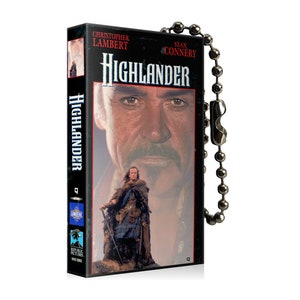 May include: A VHS tape keychain featuring the movie Highlander with Christopher Lambert and Sean Connery. The keychain is black with a silver chain.