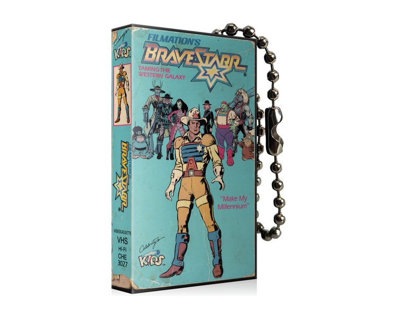 May include: A vintage VHS tape featuring the animated series "BraveStarr: Taming the Western Galaxy." The tape has a light blue cover with cartoon illustrations of characters. A silver ball chain is attached to the tape.