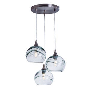 May include: A three-light pendant light fixture with a brushed nickel finish and clear glass shades. The shades have a wavy, textured design.